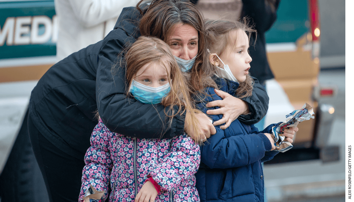 A mother wearing a mask holds her two children outside of NYU Langone Health hospital during the nightly "Clap Because We Care" cheer for medical staff and essential workers.