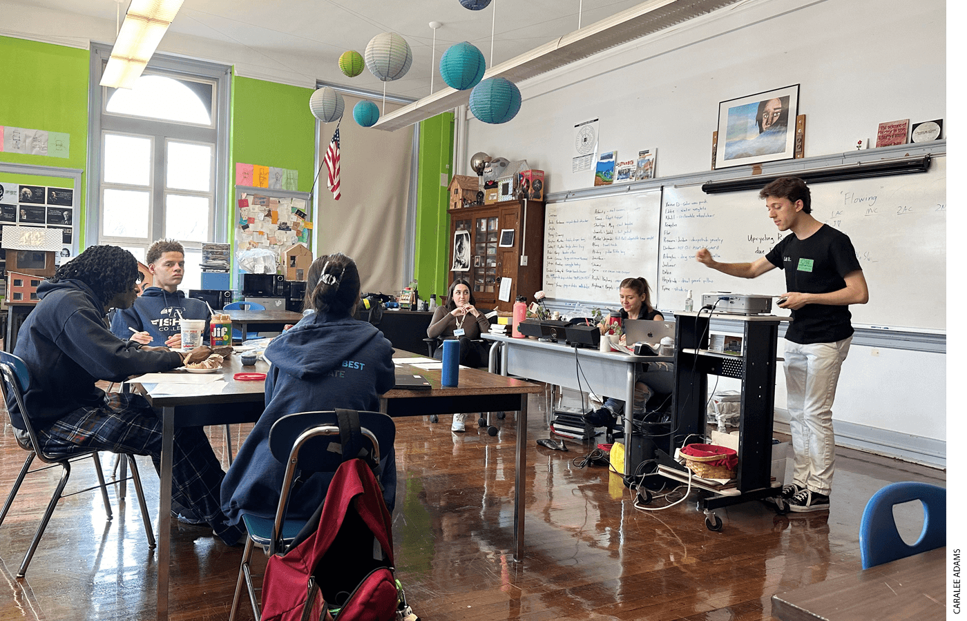 Policy debate teams are guided by coaches who are often debate league alumni, experienced college debaters, or both. Students from Boston Green Academy, with coaches Elise Green and Erica Watson, listen to mentor Jared Aimone share note-taking tips at debate practice.