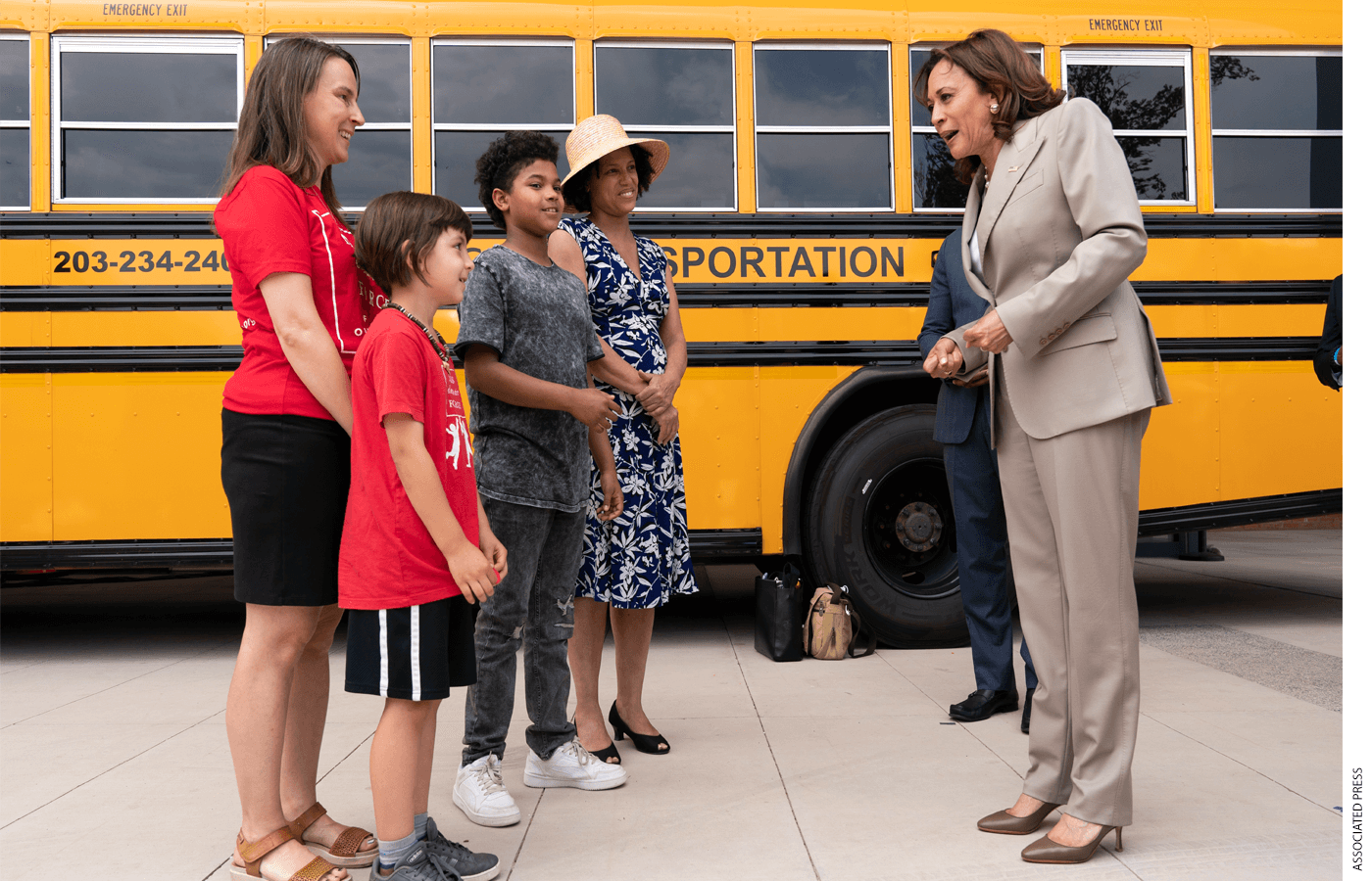 Kamala Harris speaks to students, a parent, and a teacher in front of a school bus
