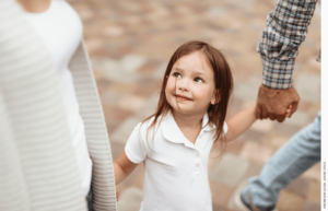 Young girl holding parents' hands, looking up at mother