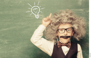 A student dressed like Albert Einstein pointing to a lightbulb drawn on a chalkboard in the background