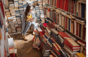 Photo of a student in a room with many books, reading her phone