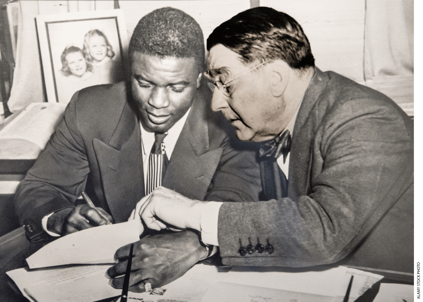 Jackie Robinson signs a contract, seated next to Branch Rickey